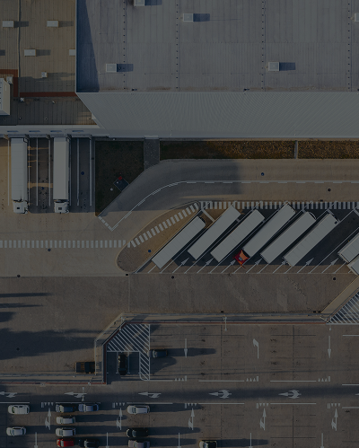 Aerial view of a logistics center with trucks parked at loading docks and a parking area for cars.